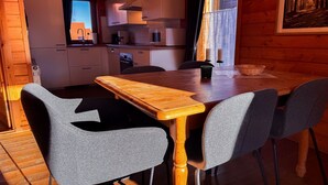 Una mesa de madera con sillas grises, una cocina al fondo y un ventanal con vistas.