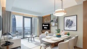 A modern hotel room with a dining area, a sofa, a TV, and a bookshelf. - Luxurious 2BD in Address Residences Opera Walk to Dubai Mall & Burj Khalifa (Dubai)