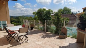An outdoor patio with a table and chairs, a grill, and a view of a swimming pool and hills. - Summer rental Villa & pool Lons le Saunier (Courlans)