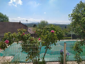 A fenced swimming pool with a view of mountains and a house in the background. - Summer rental Villa & pool Lons le Saunier (Courlans)