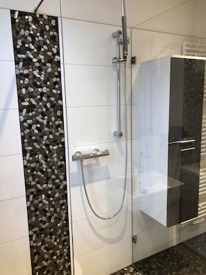 A modern bathroom with a glass shower enclosure, a black cabinet, and a pebble-patterned wall. - Vacation apartment Klaus • Comfortable vacation apartment between the old town & Elbe cycle path (Dresden)