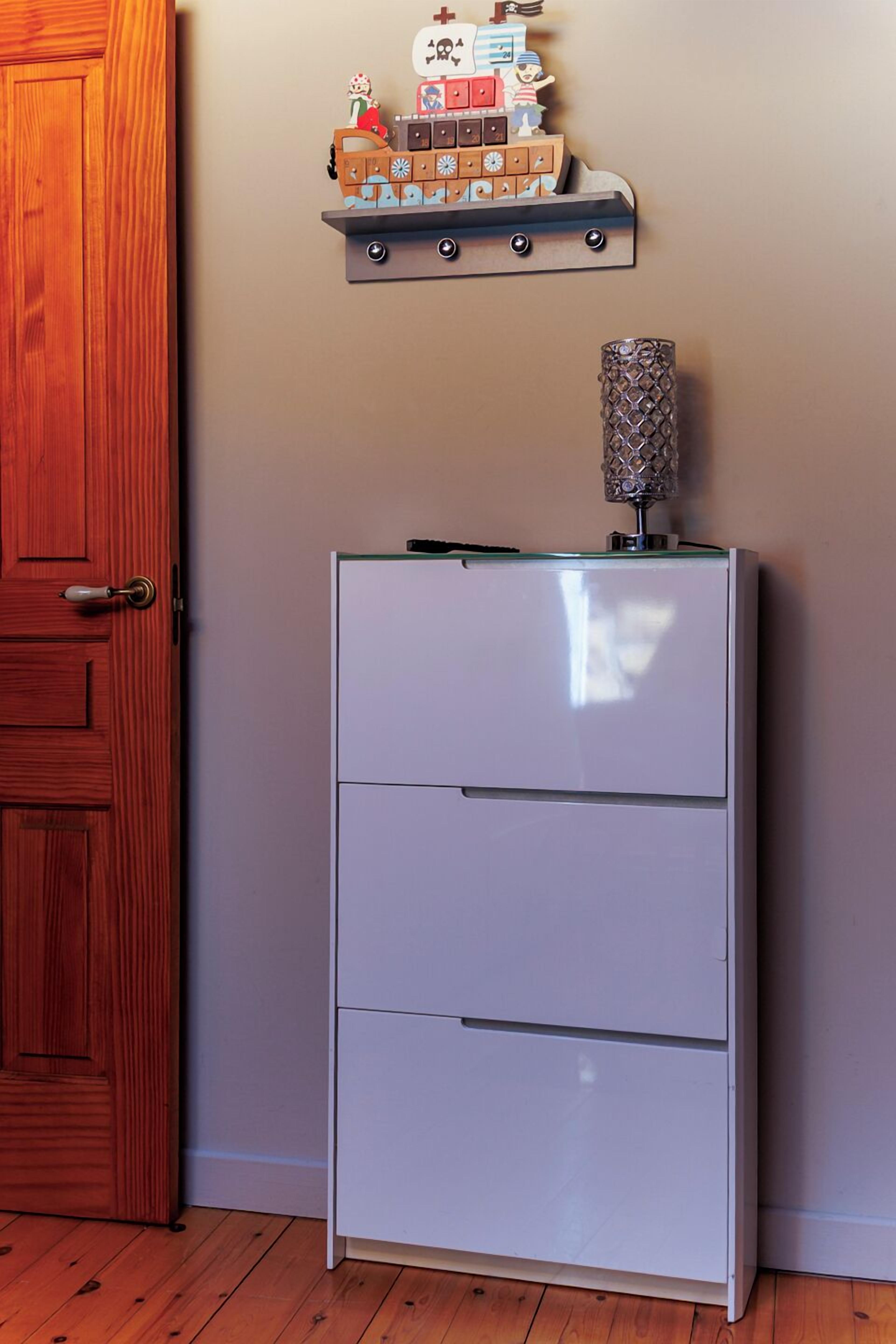 A white filing cabinet with three drawers, a wooden door, and a shelf with various items above it.