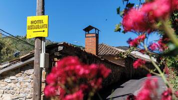 A yellow sign indicating a hotel, a stone building with a tiled roof, and a stone wall.