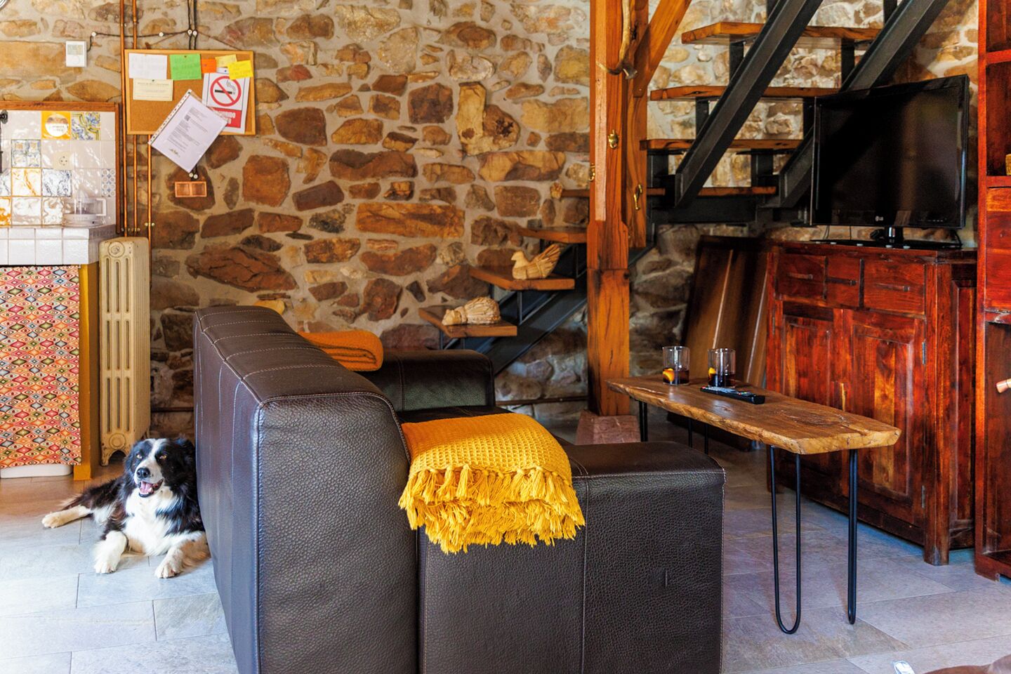 A cozy living area with a stone wall, a black leather sofa, a wooden table, and a television.