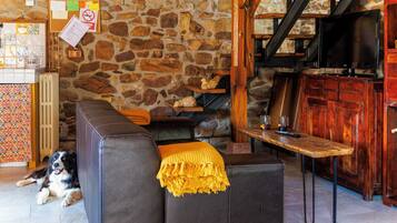 A cozy living area with a stone wall, a black leather sofa, a wooden table, and a television.