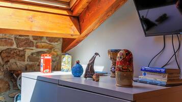 Una habitación con pared de piedra, techo de madera, televisor de pantalla plana y varios objetos decorativos, incluyendo una caja roja, un jarrón azul y una pila de libros.