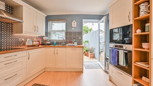A modern kitchen with white cabinets, a built-in oven, and a large window. - Lisburne Place (Torquay)