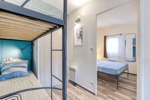 Une chambre avec un lit superposé, un lit simple, un radiateur, une œuvre d’art accrochée au mur, un miroir et une fenêtre avec des rideaux.