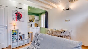 Una sala de estar con sofá, estantería, mesa de comedor y cocina al fondo.