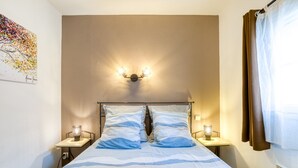 Un dormitorio con cama, lámparas de noche, una lámpara de pared y una ventana con cortinas.