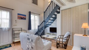 Una sala de estar con un sofá, una silla, un televisor, una lámpara y una escalera.
