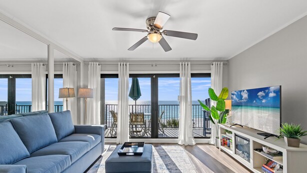 Un soggiorno moderno con divano, tavolino e televisione su un balcone con vista sull'oceano.