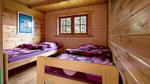 A cabin with two wooden bunk beds, a window with a view of trees, and a framed picture on the wall. - Summer cottages in Kashubia. (Dąbie)