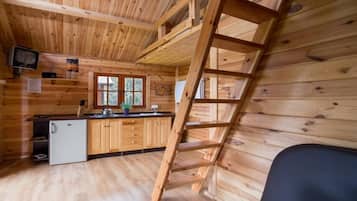 A wooden cabin interior with a kitchen, a ladder, and a small refrigerator.