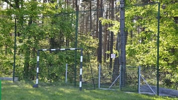 Portería de fútbol rodeada por una cerca en un césped con árboles al fondo.