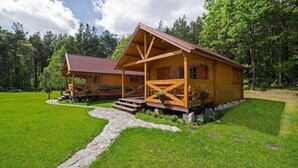 A wooden cabin with a porch, surrounded by a well-maintained lawn and stone pathway. - Summer cottages in Kashubia. (Dąbie)