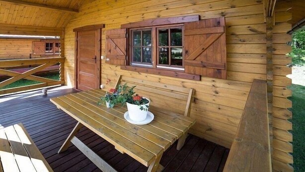 A wooden cabin with a wooden bench and table, a window with shutters, and a covered outdoor area. - Summer cottages in Kashubia. (Dąbie)