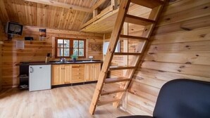 A wooden cabin interior with a kitchen area, a ladder, and a black chair. - Summer cottages in Kashubia. (Dąbie)