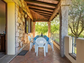 A covered outdoor patio with stone walls, a wooden ceiling, and a table with chairs. - Cozy Home Near the sea (Siniscola)