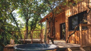 Une cabane en bois dotée d’un bain à remous, d’une terrasse en bois et d’un espace extérieur couvert agrémenté d’une pergola.