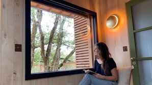 Une personne assise sur un banc en bois près d’une fenêtre, avec vue sur les arbres.