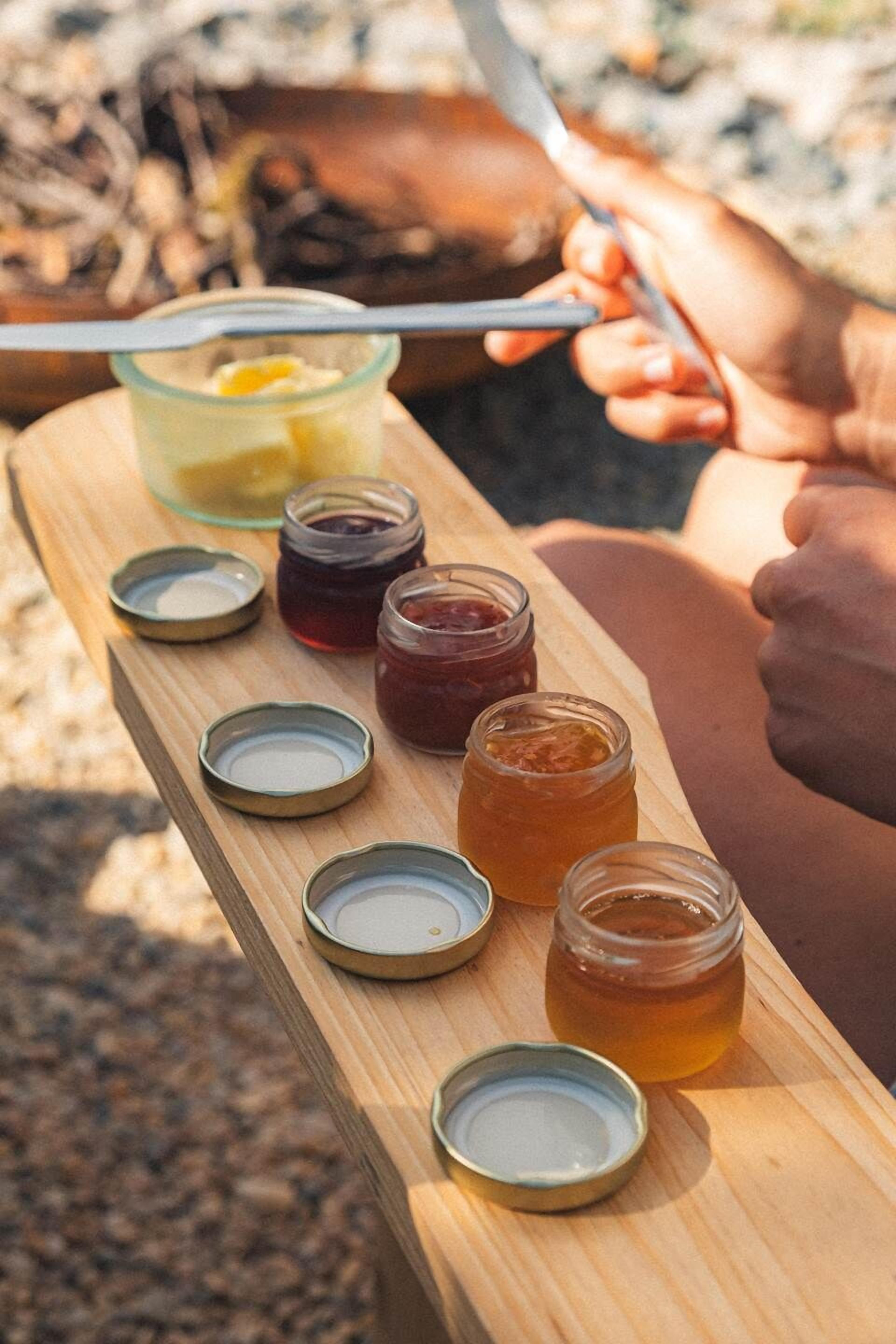 Un plateau en bois contenant divers pots de confitures et un verre de jus de citron.