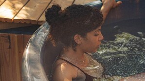 Une personne se détend dans un bain à remous, avec une table en bois et une lampe décorative en arrière-plan.