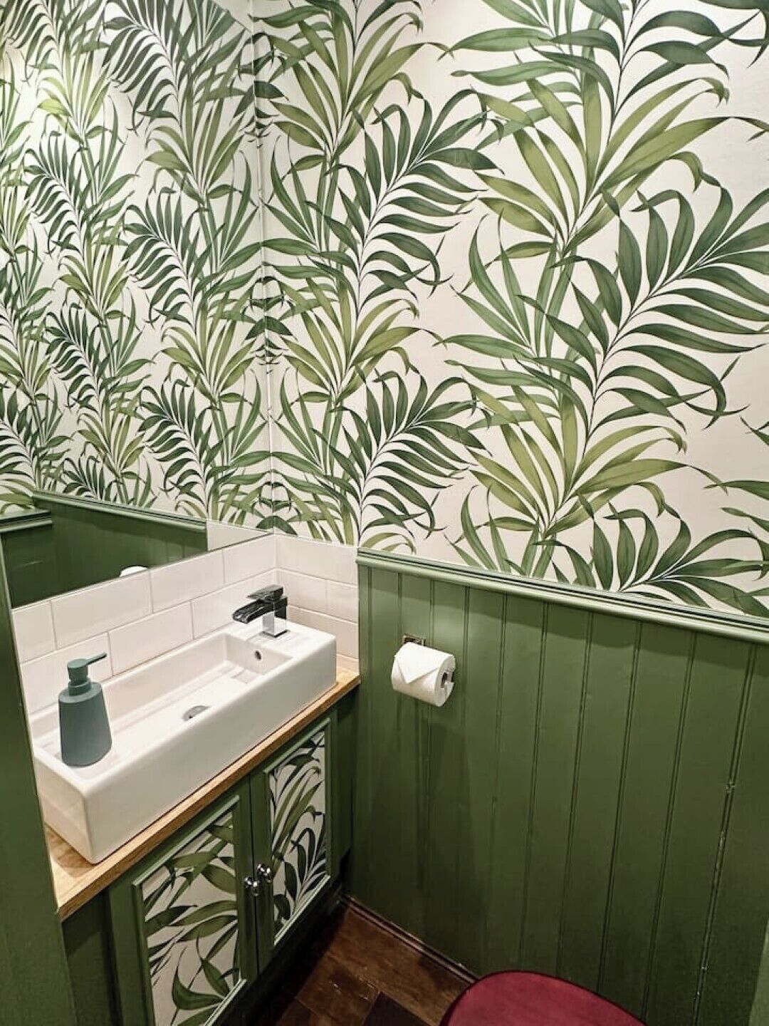 A bathroom with a green vanity, a white sink, and a mirror.
