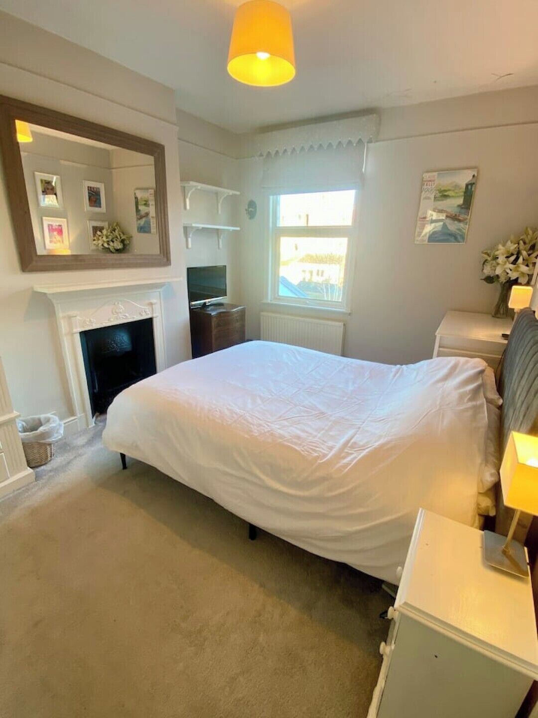 A bedroom with a large bed, a fireplace, a window with a view, and a mirror on the wall.