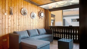 A wooden-paneled room with a sofa, a small table, decorative plates, and a view of a building through a window. - Apartment on the Main 1 with Private Terrace (Gemünden am Main)