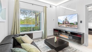 A modern living room with a large flat-screen TV, a fireplace, and a view of a castle through a window. - 1 bedroom apartment near Disney and Universal (Orlando)