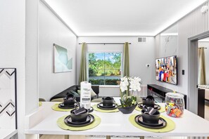 A modern hotel room with a dining area featuring black and green tableware, a potted orchid, and a snack jar. - 1 bedroom apartment near Disney and Universal (Orlando)