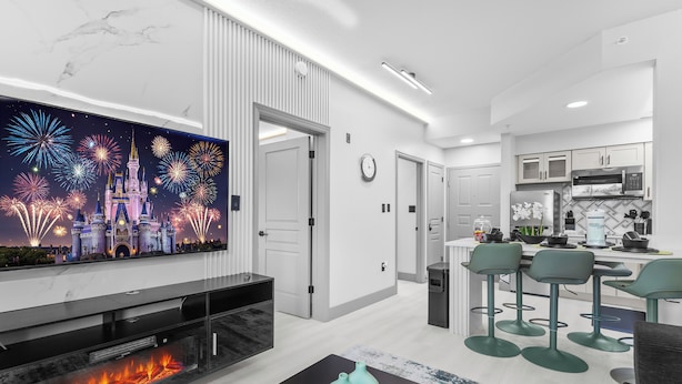A modern living room with a flat-screen TV, a fireplace, and a bar area with stools. - 1 bedroom apartment near Disney and Universal (Orlando)
