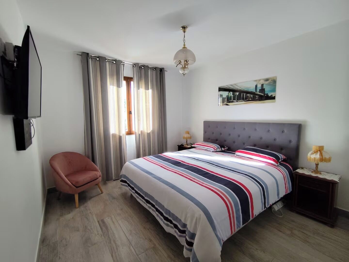 Ein Schlafzimmer mit Bett, Sessel, Fernseher und einem Fenster mit Vorhängen.