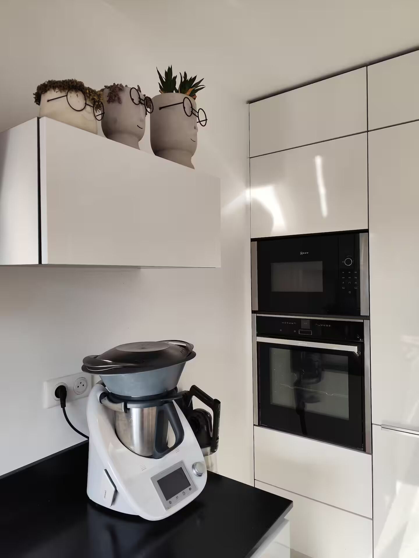 Una cocina moderna con armarios blancos, horno empotrado, microondas y cafetera sobre la encimera.