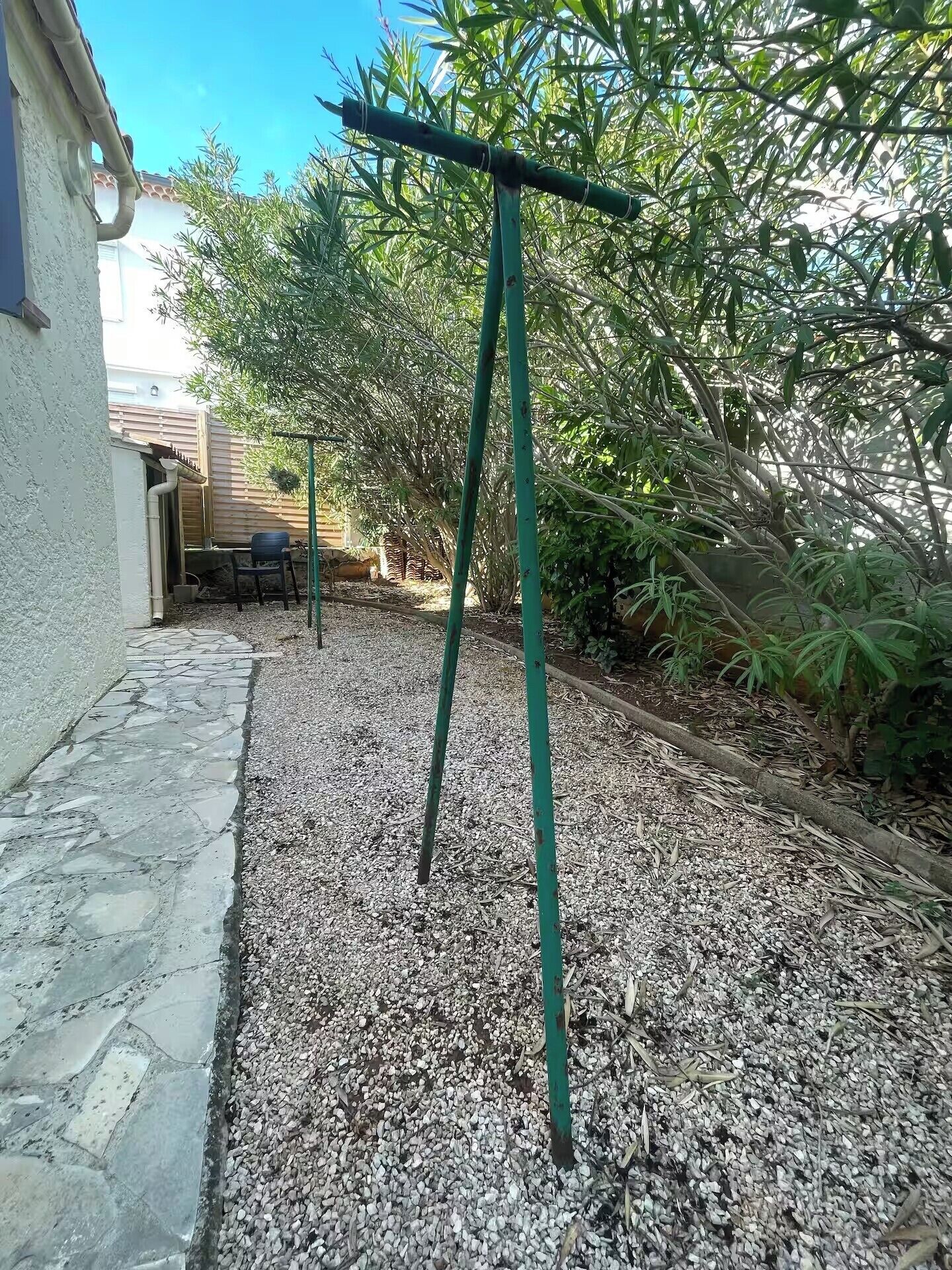 Ein Gartenbereich mit Kiesweg, grünen Metallkonstruktionen und üppigem Grün.