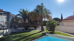 Piscina com superfície de água azul cristalina, rodeada por um gramado bem cuidado e palmeiras.