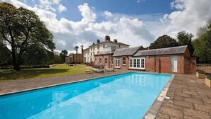 Une piscine bordée de briques, entourée d’une pelouse et d’un bâtiment à la façade en briques et doté de grandes fenêtres.