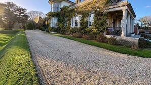 Une grande maison historique, dotée d’une allée en gravier et d’une pelouse bien entretenue.