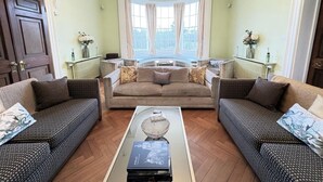 Un salon avec deux canapés à motifs, une table basse centrale et une grande fenêtre avec des rideaux.