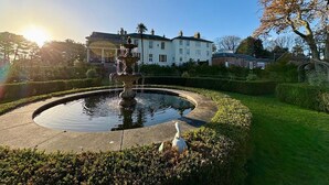 Une fontaine dans un jardin circulaire, avec un bâtiment en arrière-plan.