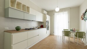 A modern kitchen with white cabinets, a wooden countertop, and a dining area with green chairs. - BDC - Tender 2Bdr apartment @Navigli area (Milan)