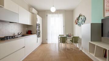 Een moderne keuken met witte kasten, een visgraatvloer, een eethoek met een tafel en stoelen, en een televisie aan de rechterkant.