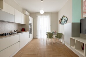 A modern kitchen with white cabinets, a herringbone floor, a dining area with a table and chairs, and a TV on the right. - BDC - Tender 2Bdr apartment @Navigli area (Milan)