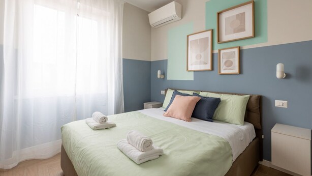 A neatly made bed with pillows, a bedside table, and a wall-mounted air conditioner. - BDC - Tender 2Bdr apartment @Navigli area (Milan)