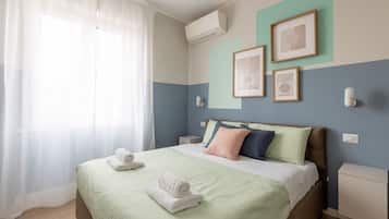 Een net opgemaakt bed met kussens, een nachtkastje en een wandgemonteerde airconditioner.