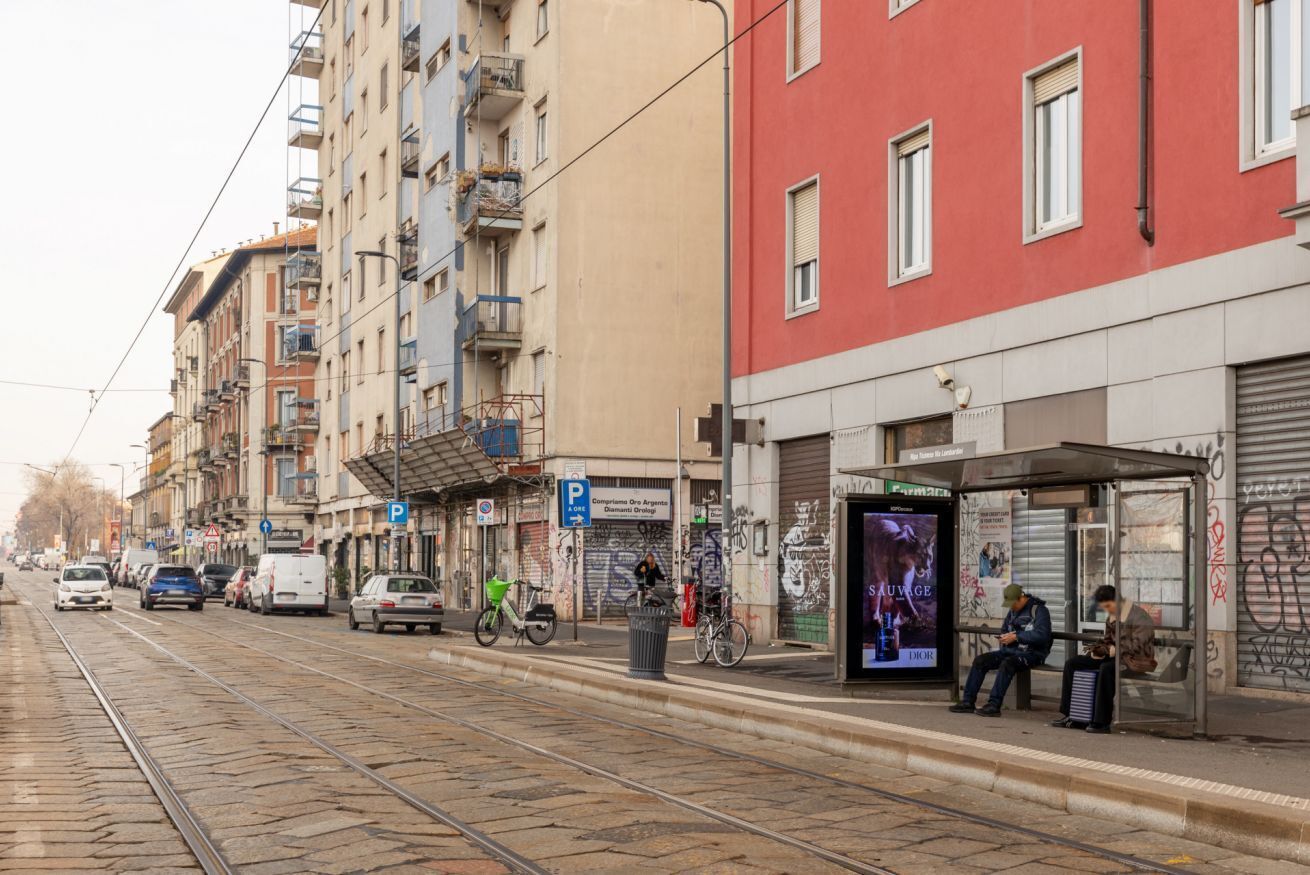 Uma linha de elétrico, um ponto de ônibus e um edifício com fachada vermelha.