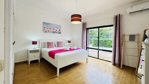Un dormitorio con cama, mesitas de noche, un cuadro, una ventana con cortinas y un equipo de aire acondicionado.