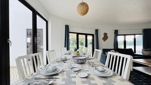 Comedor con mesa dispuesta para seis, ventanas amplias y una lámpara colgante.