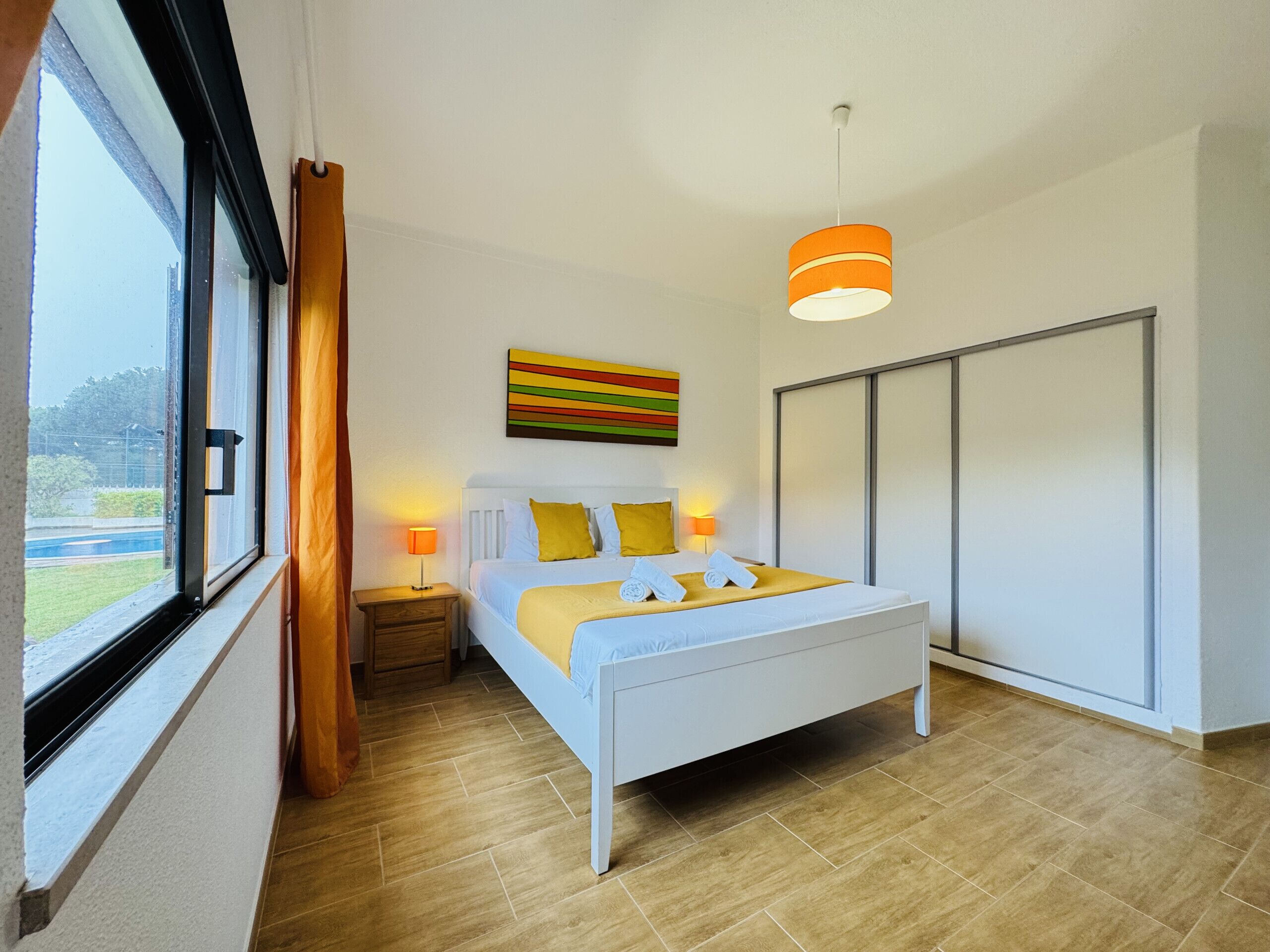Une chambre moderne avec un grand lit, des lampes de chevet, une vue sur un court de tennis et un placard à portes coulissantes.
